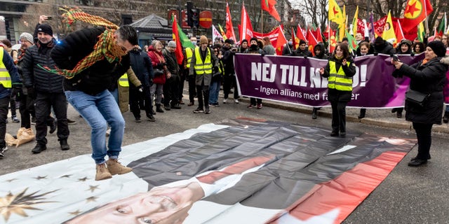 A protester prepares to jump on a banner with the image of Turkish President Recep Tayyip Erdogan during a demonstration in Stockholm on January 21, 2023. (Christine Olsson/TT Nyhetsbyrån via AP)