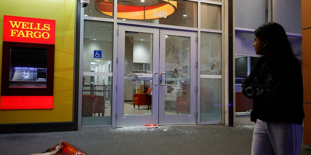 People walk by broken windows at a Wells Fargo branch following a violent protest, late Saturday, Jan. 21, 2023, in Atlanta, in the wake of the death of an environmental activist killed after authorities said the 26-year-old shot a state trooper. 