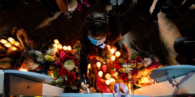 A woman writes a message on a wooden heart that displays the name of a victim at a vigil outside Monterey Park City Hall, blocks from the Star Ballroom Dance Studio, late Tuesday, Jan. 24, 2023, in Monterey Park, Calif. 