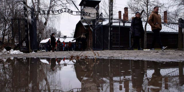 People walk next to the ''Arbeit Macht Frei" (Work Sets You Free) gate at the former Nazi German concentration and extermination camp Auschwitz-Birkenau in Oswiecim, Poland, Thursday, Jan. 26, 2023.