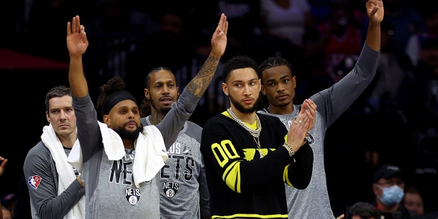 Patty Mills #8 and Ben Simmons #10 of the Brooklyn Nets celebrate teammate Kyrie Irving's three-point shot while on the bench in the first half against the Philadelphia 76ers at the Wells Fargo Center on March 10, 2022 in Philadelphia, Pennsylvania.