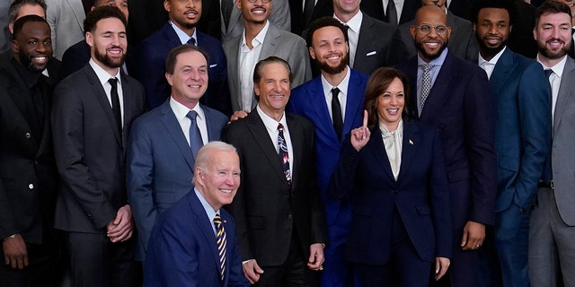 President Joe Biden kneels during a group photo with Vice President Kamala Harris and members of the 2022 NBA Champion, Golden State Warriors during an event in the East Room of the White House, Tuesday, Jan. 17, 2023, in Washington.
