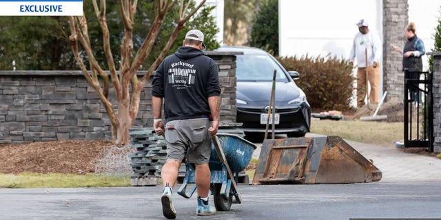 Man presumably working for a landscaping company moving material around the worksite at President Biden's vacation home in Delaware. President Biden is having a wall built around his beach house despite calls against a wall at the southern border.