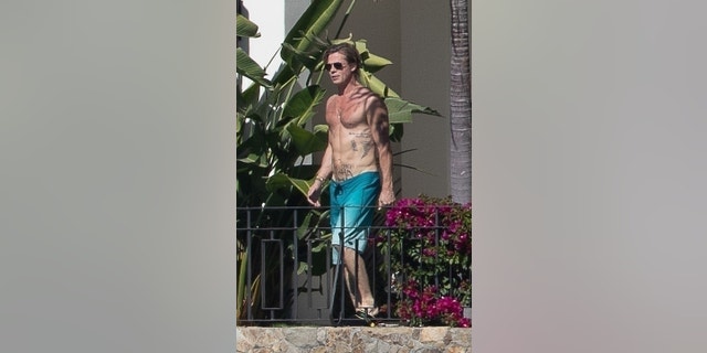 Brad Pitt shows off his tattoos while walking around the pool in a pair of blue swim trunks.