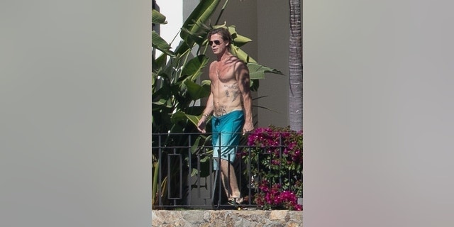 Brad Pitt montre ses tatouages ​​en se promenant autour de la piscine dans un maillot de bain bleu.