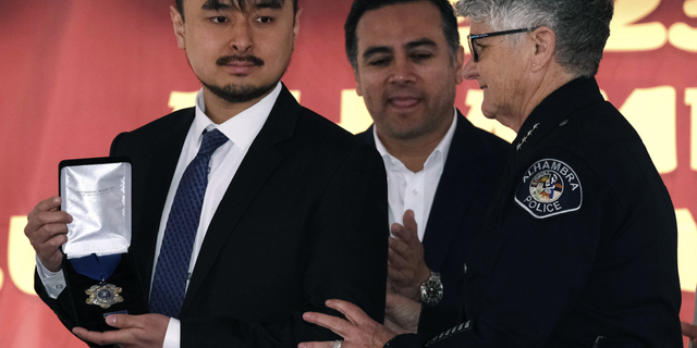 Brandon Tsay displays a Metal of Courage award after being presented to him by Alhambra Police Chief Kelley Fraser, right, on Sunday, Jan. 29, 2023 in Alhambra, California