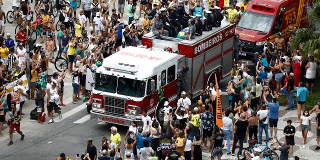 Los fanáticos se alinean en la calle mientras los bomberos cargan el ataúd de la leyenda del fútbol brasileño Pelé desde el estadio Vila Belmiro de su antiguo club, el Santos.