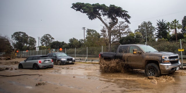 A truck tows a car that got stuck in the mud as a result of San Ysidro Creek overflowing due to heavy rainfall in the area on Jan. 10, 2023, in Montecito, California. 