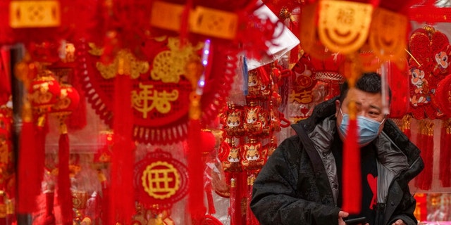 E Mann, deen eng Gesiichtsmaske droen, Geschäfter fir Chinesesch Mound-Neijoersdekoratiounen an engem Geschäft zu Peking, Samschdeg, Jan.  7, 2023.