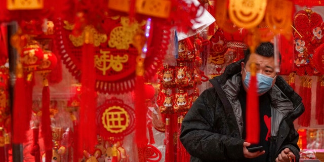 A man wearing a face mask shops for Chinese Lunar New Year decorations at a pavement store in Beijing, Saturday, Jan. 7, 2023. China has suspended or closed the social media accounts of more than 1,000 critics of the government's policies on the COVID-19 outbreak, as the country moves to further open up. 