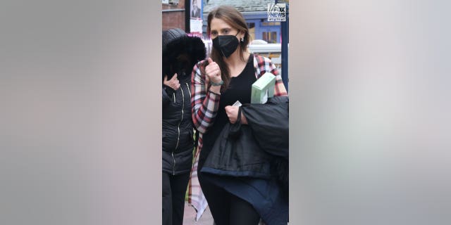 Woman in a plaid shirt and face mask clutches her coat and a box of tissues