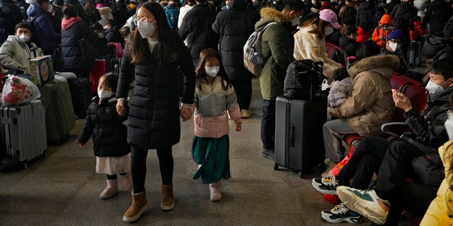 Uma mulher e crianças usando máscaras passam por viajantes mascarados e esperam em um saguão de embarque para pegar seus trens na Estação Ferroviária Oeste de Pequim no domingo, 15 de janeiro de 2023.