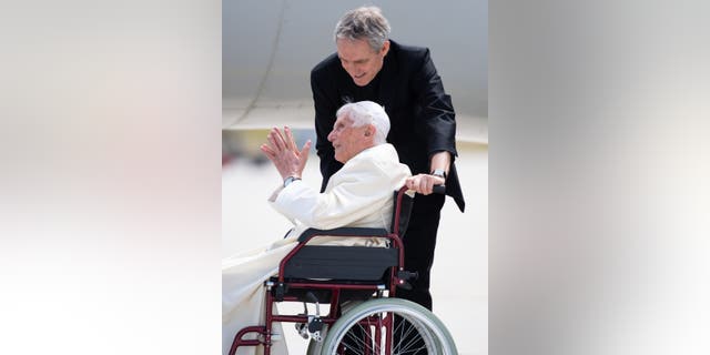 Georg Gänswein and Pope Emeritus Benedict XVI stand together at Munich Airport for a photo.