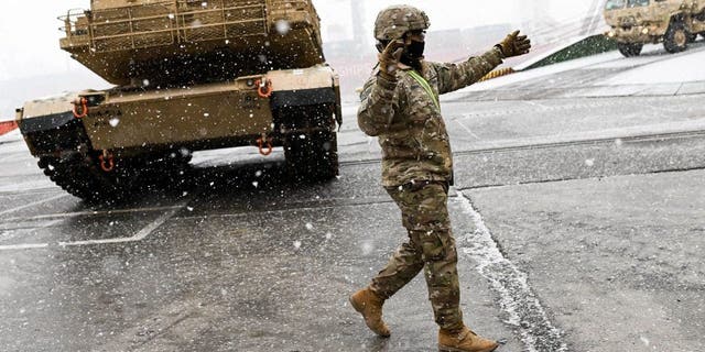 A U.S. Army soldier signals the way to a M1A2 Abrams battle tank that will be used for military exercises by the 2nd Armored Brigade Combat Team, at the Baltic Container Terminal in Gdynia, Poland, on Dec. 3, 2022. 