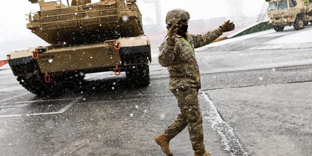 A U.S. Army soldier signals the way to a M1A2 Abrams battle tank that will be used for military exercises by the 2nd Armored Brigade Combat Team, at the Baltic Container Terminal in Gdynia, Poland, on Dec. 3, 2022.