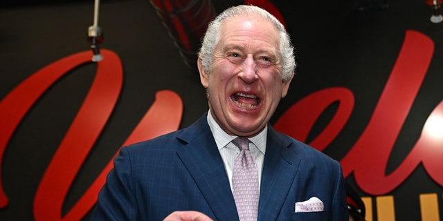 King Charles laughs in a navy suit and light pink tie while in Manchester