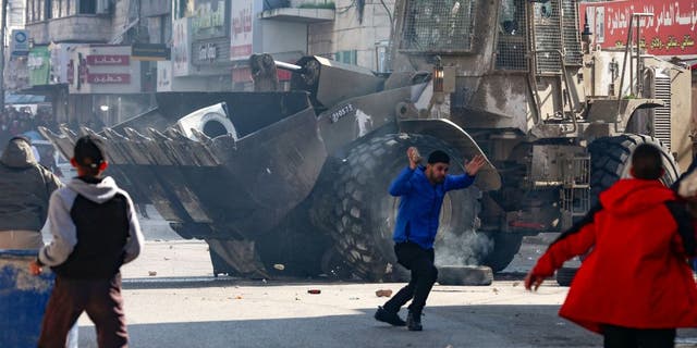 Palestinians hurl rocks at an Israeli army bulldozer, during confrontations in the occupied-West Bank city of Jenin, on January 26, 2023. (JAAFAR/AFP via Getty Images)