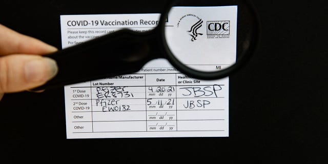 A photo of a hand using a magnifying glass to check the authenticity of s Covid-19 vaccine card, taken on August 15, 2021. 