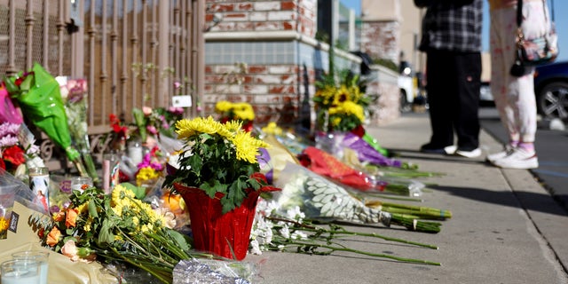 People stand at a makeshift memorial outside the scene of a deadly mass shooting at a ballroom dance studio in Monterey Park, California. An eleventh person has died and 10 more were injured at the studio near a Lunar New Year celebration on Saturday night.