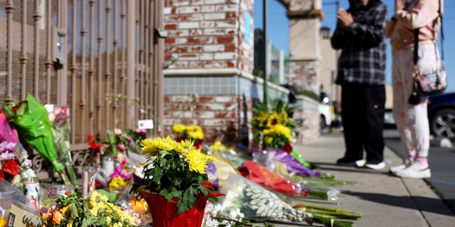 People stand at a makeshift memorial outside the scene of a deadly mass shooting at a ballroom dance studio in Monterey Park, California. An eleventh person has died and 10 more were injured at the studio near a Lunar New Year celebration on Saturday night.