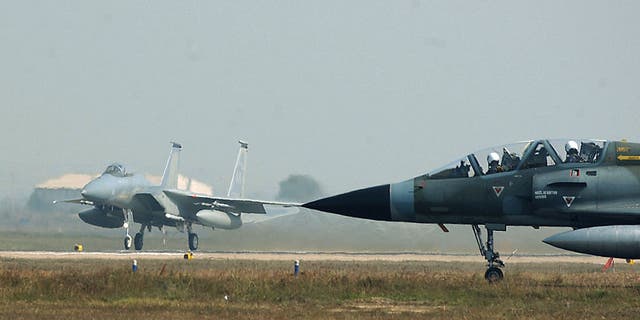 Nesta foto divulgada fornecida pela Força Aérea dos EUA, um Mirage da Força Aérea Indiana espera para taxiar para a pista (R) enquanto um F-15C Eagle (L) da Força Aérea dos EUA decola em 13 de fevereiro de 2004 na Estação da Força Aérea de Gwalior, na Índia . 