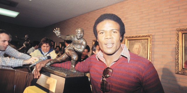 USC's Charles White, winner of the 1979 Heisman Trophy, puts his arm around the same trophy won by O.J. Simpson during press conference 12/3. White, the third Trojan to win the award, finished the regular season with 1,803 yards on the ground, the most in the nation.