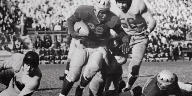 An 82-yard march in the final five minutes of play earned the UCLA football team a 13-13 tie with Oregon State College in a wide-open battle staged before 40,000 fans. Statistics showed the two teams played on practically an even basis with a slight advantage to UCLA. Photo shows UCLA right half Jackie Robinson (#28) being stopped after receiving an 8-yard pass from teammate Kenny Washington. Oregon State's right tackle Walter Jelsma is shown at #56.