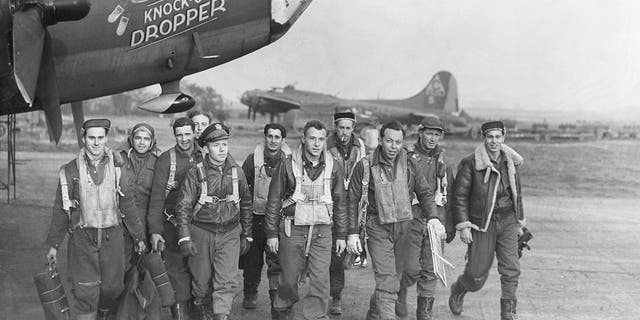 The crew of the B-17 Flying Fortress Knock-out Dropper bomber walk away from their plane. At center, wearing a flak jacket, is pilot John P. Manning. To the left of Manning, wearing a brimmed cap, is copilot George T. Mackin.