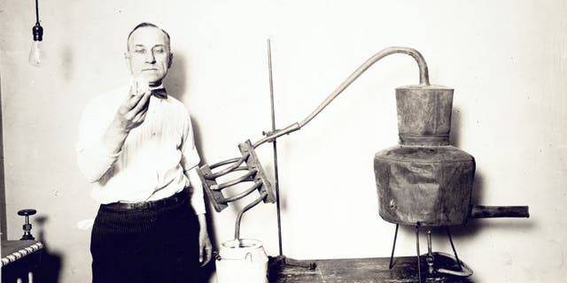 Moonshine confiscated by the Internal Revenue Bureau photographed at the Treasury Department between 1921 and 1932. Man standing by, looking at the contents of the glass. Nearly 600,000 Americans were arrested by Prohibition agents in the 1920s.