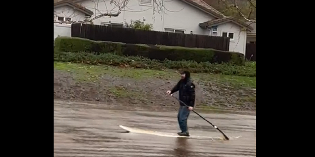 A man is seen paddleboarding through a flooded backyard in Goleta, California, following rainfall there.