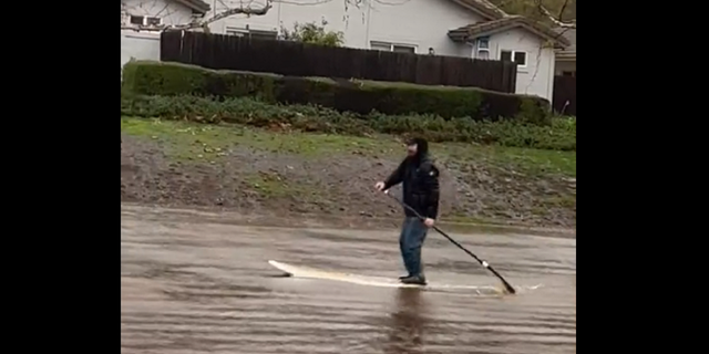 A man is seen paddleboarding through a flooded backyard in Goleta, California, following rainfall there.