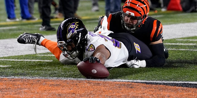 El corredor de los Baltimore Ravens, JK Dobbins, a la izquierda, anota mientras el apoyador de los Cincinnati Bengals, Markus Bailey, defiende en la primera mitad de un partido de playoffs de la NFL en Cincinnati, el domingo 15 de enero de 2023.