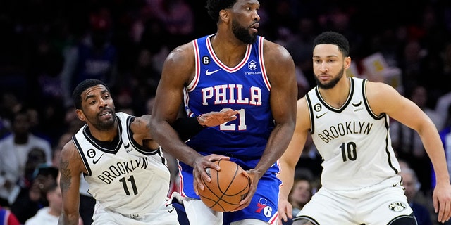 Joel Embiid, centro, de los 76ers de Filadelfia, intenta aferrarse al balón contra Kyrie Irving, izquierda, y Ben Simmons, de los Nets de Brooklyn, durante la primera mitad de un partido de baloncesto de la NBA, el miércoles 25 de enero de 2023, en Filadelfia. 