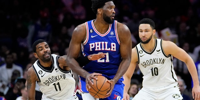 Philadelphia 76ers' Joel Embiid, center, tries to hang onto the ball against Brooklyn Nets' Kyrie Irving, left, and Ben Simmons during the first half of an NBA basketball game, Wednesday, Jan. 25, 2023, in Philadelphia.