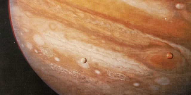 The planet Jupiter, 1979. Taken from Voyager 1 at 20 million kilometres this pictures shows the Great Red Spot, a storm that has been raging for hundreds of years, and two of Jupiter's moons - Io over the Red Spot and Europa. 