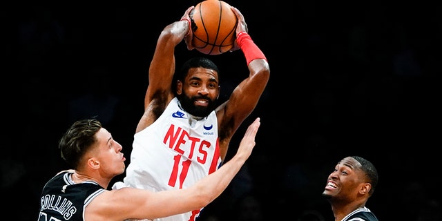 Brooklyn Nets' Kyrie Irving (11) passes away from San Antonio Spurs' Zach Collins and Malaki Branham during the first half of an NBA basketball game, Monday, Jan. 2, 2023, in New York. 