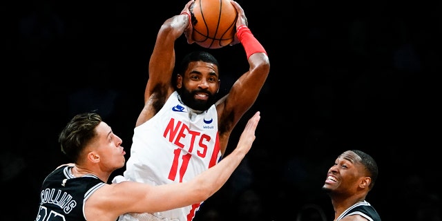 Kyrie Irving (11) de los Nets de Brooklyn muere a manos de Zach Collins y Malaki Branham de los Spurs de San Antonio durante la primera mitad de un partido de baloncesto de la NBA, el lunes 2 de enero de 2023, en la ciudad de Nueva York. 