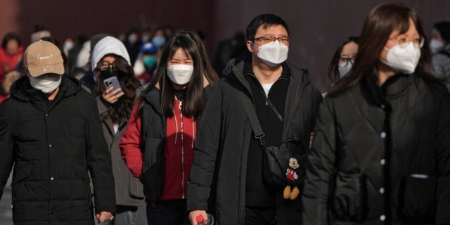 People wearing face masks walk along a street in Beijing, Friday, Jan. 6, 2023.