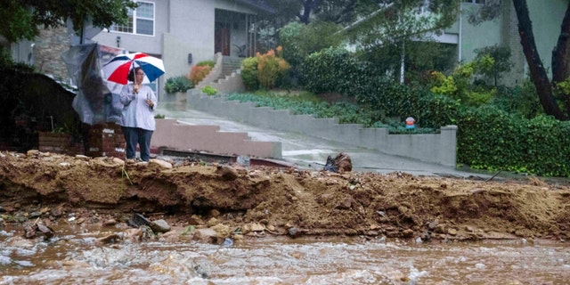 A resident keeps watch on Fredonia Drive in Studio City, Calif., where a mudslide is blocking the road during a rain on Jan. 10, 2023.   