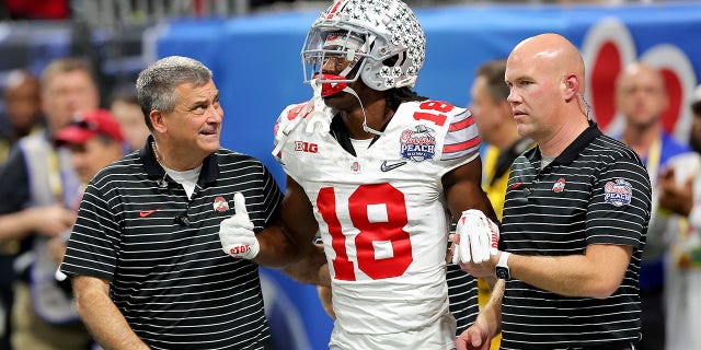 Ohio State Buckeyes takımından Marvin Harrison Jr. (18), Atlanta'daki Mercedes-Benz Stadyumu'ndaki Chick-fil-A Peach Bowl'da Georgia Bulldogs'a karşı üçüncü çeyrekte sakatlandıktan sonra sahadan çıkmasına yardım ediliyor. ,