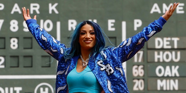 La seis veces campeona femenina de la WWE, Sasha Banks, levanta los brazos después de lanzar el primer lanzamiento antes del partido entre los Medias Rojas de Boston y los Medias Blancas de Chicago en el Fenway Park el 8 de mayo de 2022 en Boston.