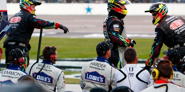 Zwart geklede pitbemanningsleden wachten op de muur om Jimmie Johnson's Lowe's Chevy te onderhouden laat in de NASCAR AAA Texas 500 op Texas Motor Speedway op 7 november 2010 in Fort Worth, Texas.