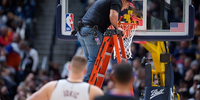 A worker uses a level to check the rim after it bent during a dunk by Boston Celtics center Robert Williams III, Sunday, Jan. 1, 2023, in Denver.