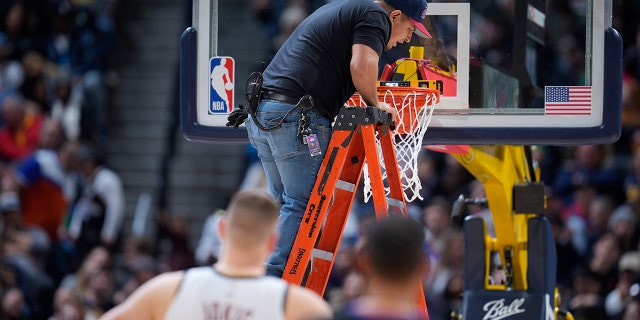 A worker uses a level to check the rim after it bent during a dunk by Boston Celtics center Robert Williams III, Sunday, Jan. 1, 2023, in Denver.