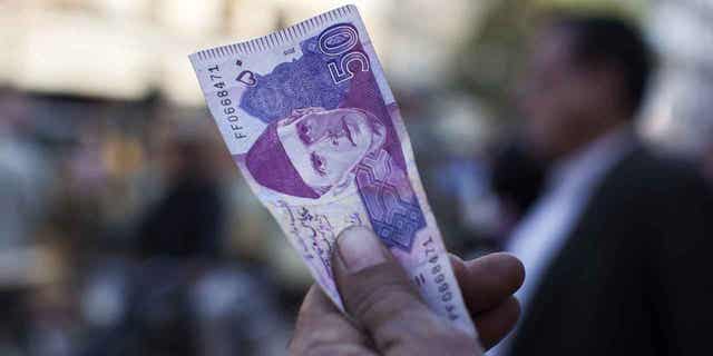 A roadside money changer holds up a Pakistani Fifty Rupee banknotes in Karachi, Pakistan, on Dec. 14, 2017. Pakistan's rupee has plunged in comparison to the U.S. dollar after the government agreed to comply with the IMF.
