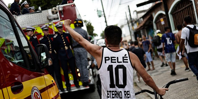 Un aficionado del Santos luce una camiseta de Pele mientras los bomberos se llevan el ataúd de Pele.