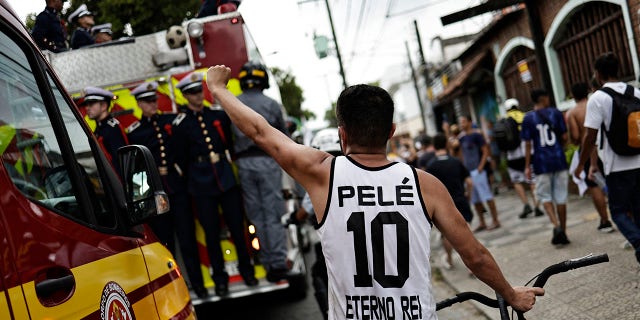 Un aficionado del Santos luce una camiseta de Pele mientras los bomberos se llevan el ataúd de Pele.