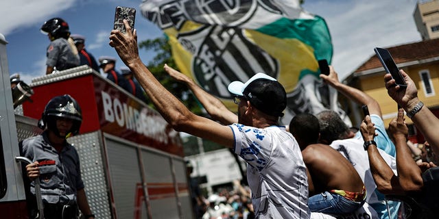Los hinchas son fotografiados mientras la leyenda del fútbol brasileño, Pelé, es transportado por los bomberos desde el estadio Vila Belmiro de su antiguo club, el Santos.