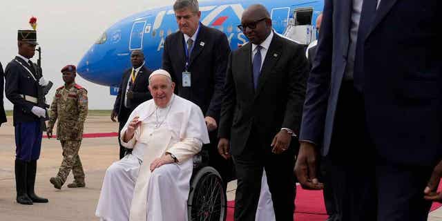 Pope Francis on a wheelchair is flanked by Congolese Prime Minister Sama Lukonde, center right, as he arrives in Kinshasa, Democratic Republic of the Congo, Tuesday, Jan. 31, 2023 to start his six-day pastoral visit to Congo and South Sudan where he'll bring a message of peace to countries riven by poverty and conflict.