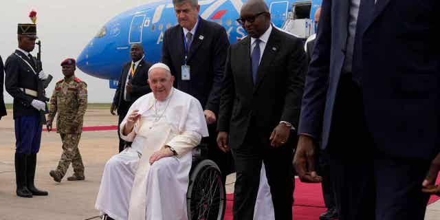 Pope Francis on a wheelchair is flanked by Congolese Prime Minister Sama Lukonde, center right, as he arrives in Kinshasa, Democratic Republic of the Congo, Tuesday, Jan. 31, 2023 to start his six-day pastoral visit to Congo and South Sudan where he'll bring a message of peace to countries riven by poverty and conflict.